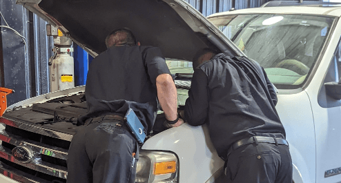 Two auto mechanics working on a engine of a white pickup truck. Concept image of Bob's Automotive's auto repair & maintenance services.